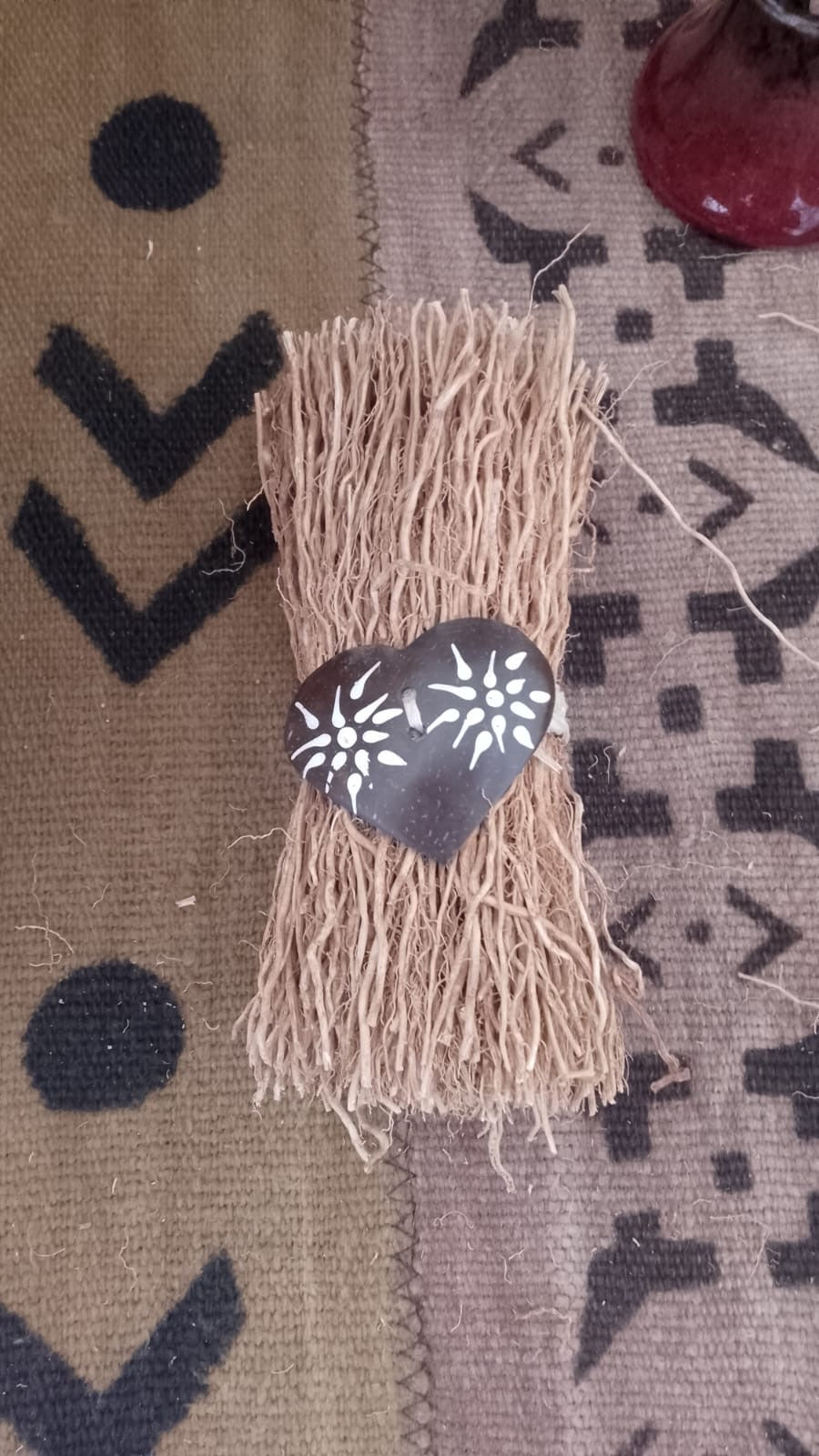 Détail des motifs floraux blancs peints main sur coque de coco naturelle du fago coco, cœur décoratif en vétiver naturel bohème et éco-responsable